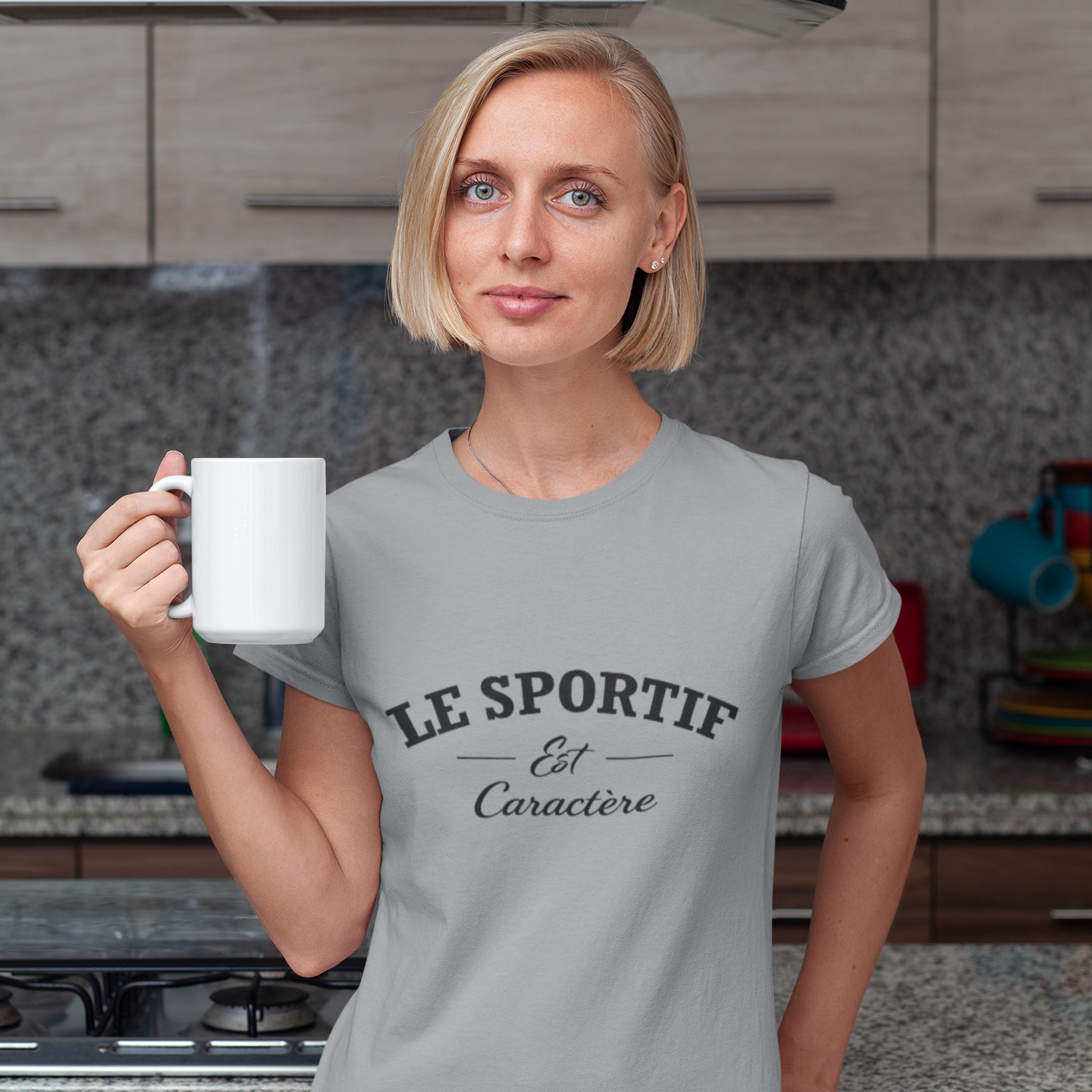 Woman holding a white mug in a kitchen wearing a gray t-shirt with text.