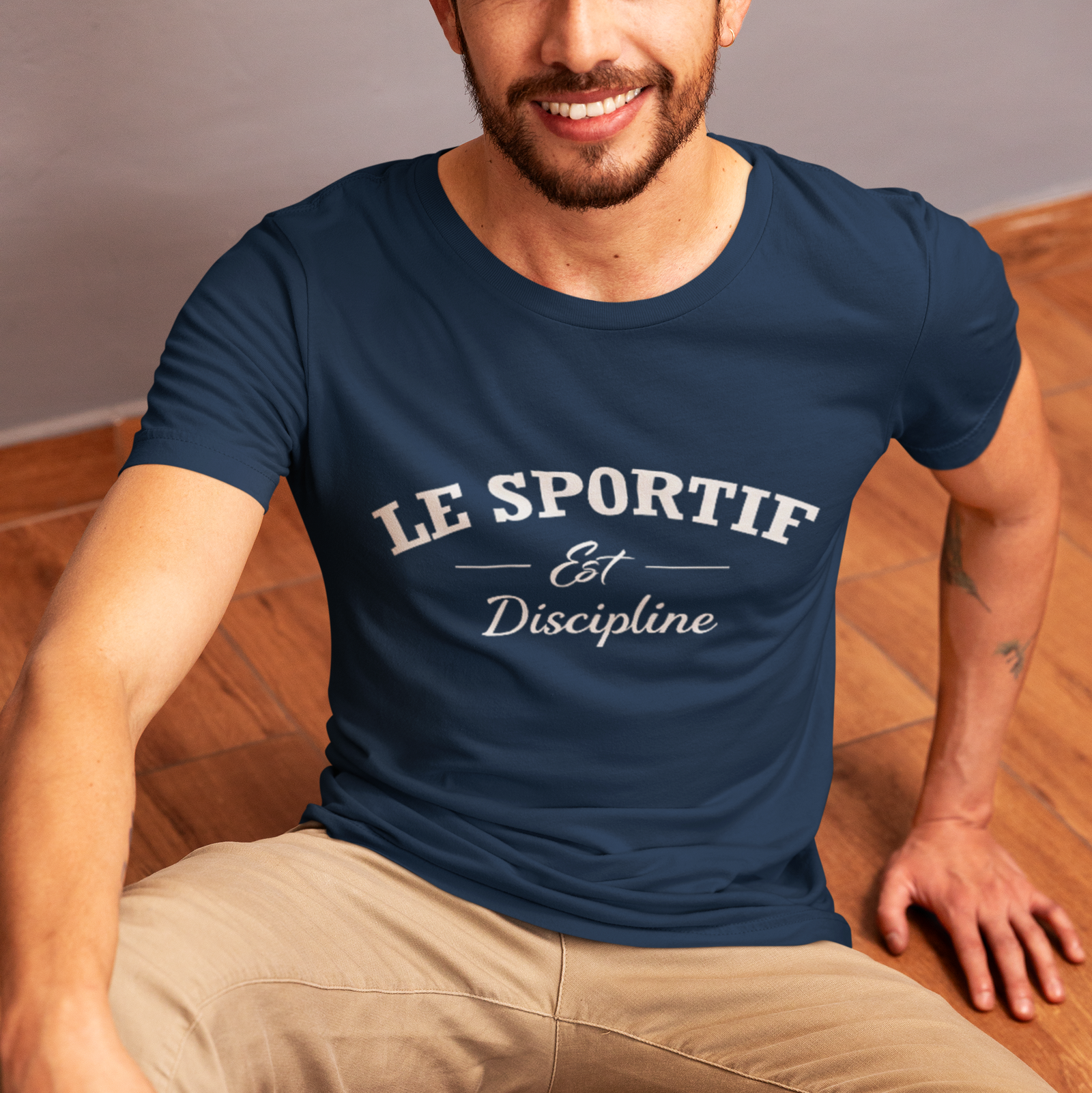 Man wearing a navy blue 'LE SPORTIF Est Discipline' t-shirt sitting on a wooden floor.