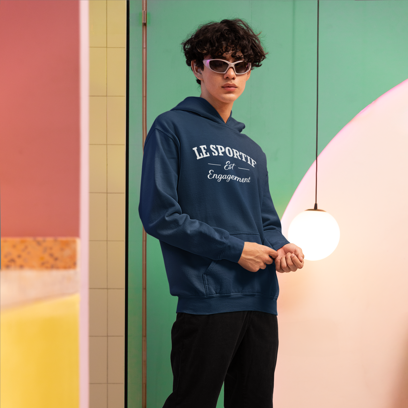 Person wearing a blue hoodie with text, black pants, and white shoes in a colorful indoor setting.