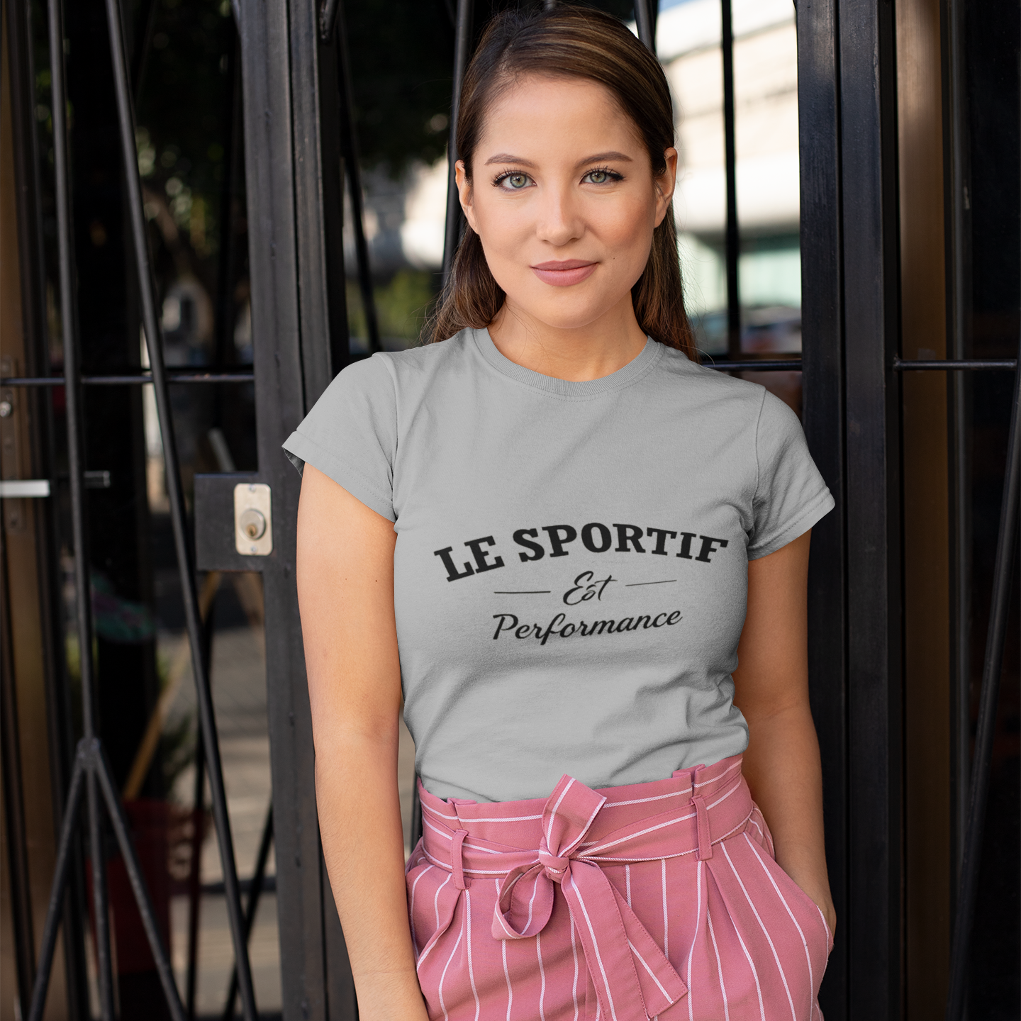 Woman wearing a gray 'Le Sportif' t-shirt and pink shorts standing outdoors.