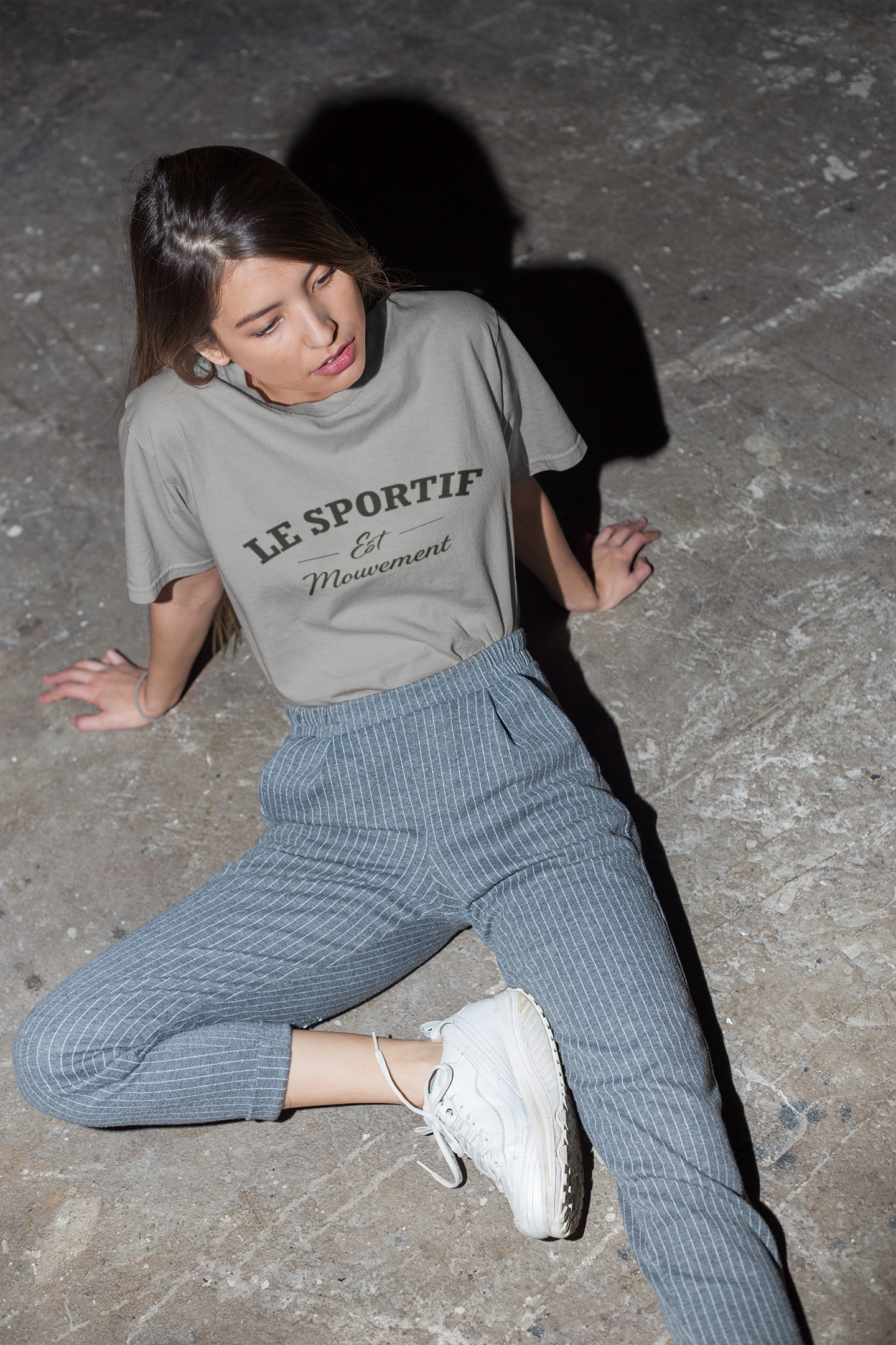Woman wearing a 'Le Sportif' t-shirt sitting on a concrete floor.